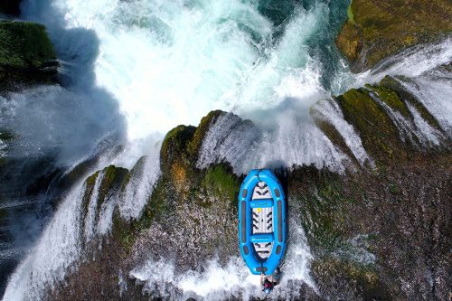 group of people doing white water rafting activity on wild river with waterfall